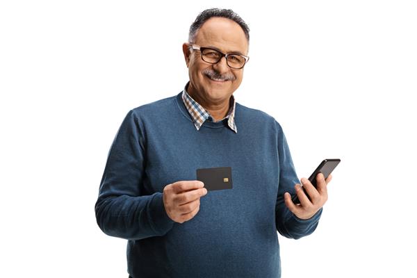 مرد مسن شاد با یک کارت اعتباری و یک تلفن همراه که به دوربین جدا شده در پس‌زمینه سفید لبخند می‌زند