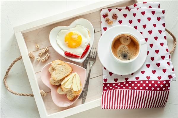 صبحانه در روز ولنتاین صبحانه برای عزیزانتان در سینی یک فنجان قهوه و دو بشقاب به شکل قلب با تخم مرغ و نان تست و یک نوشته I love you نمای از بالا