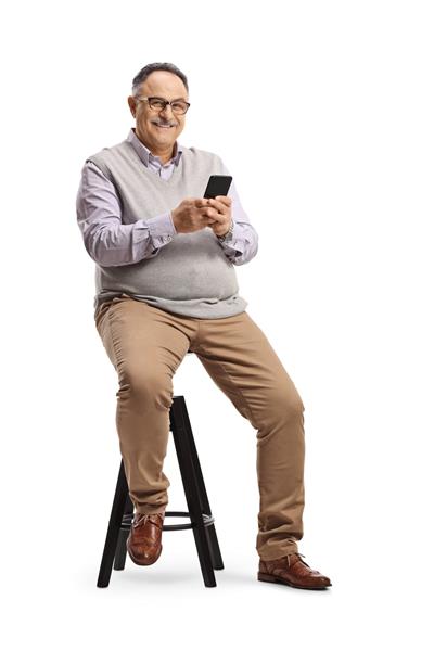 مرد بالغی که روی صندلی نشسته و یک تلفن همراه جدا شده روی پس‌زمینه سفید در دست دارد