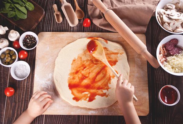 کودک در آشپزخانه خانه پیتزا درست می کند نمای بالا