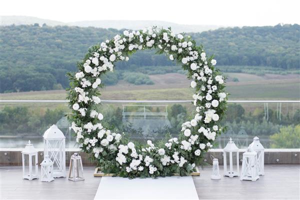 مراسم عروسی طاق عروسی بسیار زیبا و شیک تزئین شده با گل های متنوع و تازه ایستاده در باغ روز عروسی تزئینات گل های تازه عروسی گل صد تومانی