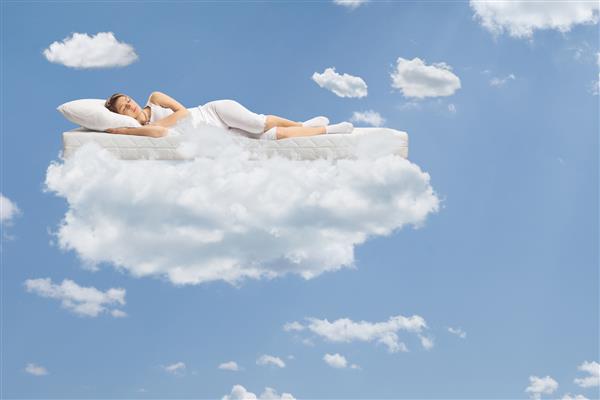 زن جوانی که روی یک تشک شناور در میان ابرها و آسمان آبی خوابیده است