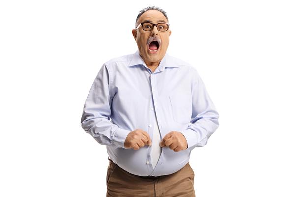 مرد شوکه شده با شکم بزرگ که سعی می کند دکمه پیراهن جدا شده در پس زمینه سفید را ببندد