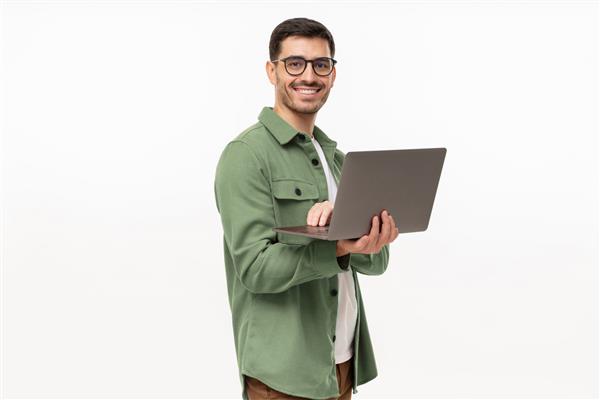 پرتره تاجر جوان مدرن که لپ تاپ در دست ایستاده و با لبخند شاد به دوربین نگاه می کند جدا شده روی خاکستری