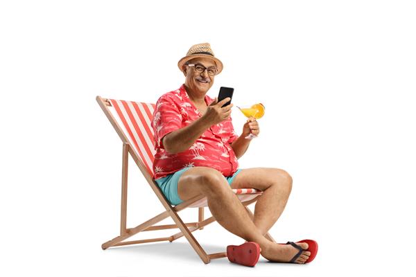 مرد بالغ نشسته روی یک صندلی ساحلی با یک گوشی هوشمند و یک کوکتل جدا شده در پس زمینه سفید