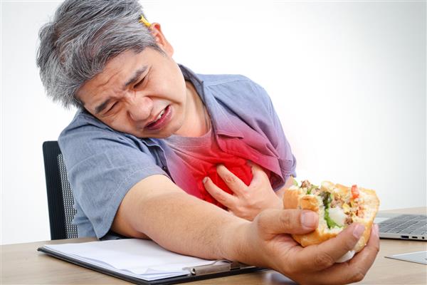 مرد چاق آسیایی هنگام کار پشت میزتان همبرگر بخورید گرفتگی قفسه سینه درد حاد شدید قلب مفهوم چاقی خطر بیماری قلبی و دیابت وجود دارد