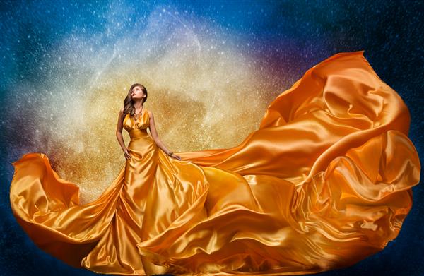 مدل مد لباس طلایی بر روی پس زمینه آسمان شب معجزه رقص زن مجلل با لباس ابریشمی بلند و نگاه کردن به ستاره ها