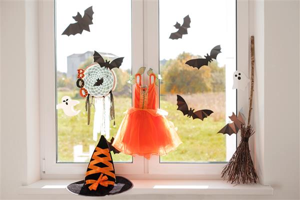 لباس کارناوال جادوگر با خفاش کلاه و جارو روی طاقچه روی پنجره آویزان است آماده سازی لباس برای جشن بالماسکه هالووین دکوراسیون اتاق روز آفتابی