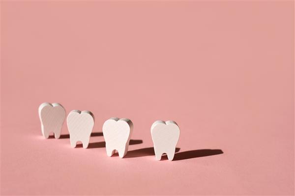 چهار دندان مصنوعی در یک ردیف روی پس زمینه صورتی با سایه عمیق ایستاده اند - مفهوم سلامت دندان محصولات بهداشتی دندان مدل دندان انسان