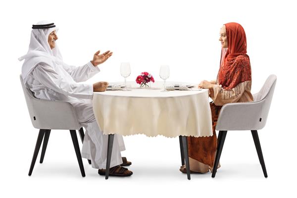 مرد عرب در حال صحبت با زنی با حجاب نشسته روی میز رستوران جدا شده در زمینه سفید