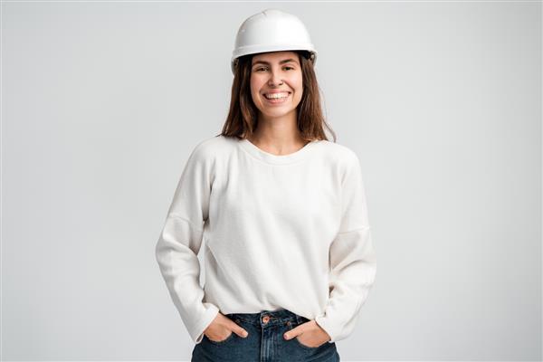 پرتره زن مهندس جوان با کلاه ایمنی سفید و لبخند دندانی در استودیو عکس جدا شده در پس زمینه سفید