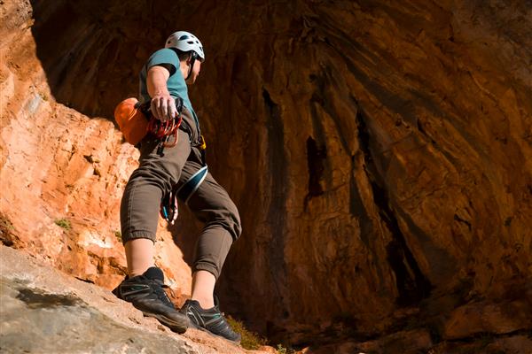 مردی به صخره نوردی مشغول است قبل از تمرین در مقابل پس زمینه یک غار قرمز زیبا می ایستد کوهنورد سبک زندگی فعالی را دنبال می کند و درگیر ورزش های شدید در یونان غارهای دوقلو است