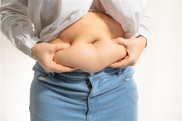 هیکل چاق زن با چین های چربی روی شکم بدون کمر وجود سلولیت اضافه وزن زنی با شکم برهنه شلوار جین کوچک و پیراهن سفید با شکم چاق