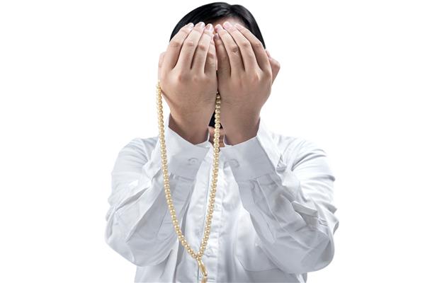 مرد مسلمان آسیایی در حال دعا با مهره های نماز بر روی دست هایش جدا شده روی پس زمینه سفید