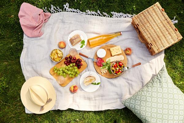 مفهوم اوقات فراغت و غذا خوردن - نزدیک از غذا نوشیدنی و سبد پیک نیک روی پتو روی چمن در پارک تابستانی