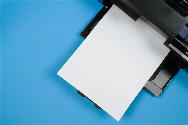 نمای بالای چاپگر و یک صفحه خالی کاغذ a4 روی پس‌زمینه آبی