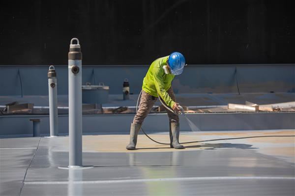 یک کارگر مرد که یک تفنگ اسپری صنعتی را در دست دارد که برای سطح مخزن صفحه پشت بام روی رنگ و پوشش صنعتی فولادی استفاده می شود