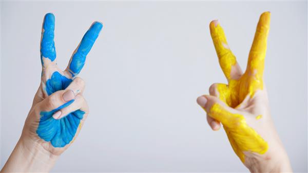 عکس استوک نمای نزدیک از دو دست زن که با رنگ‌های آبی و زرد پرچم ملی اوکراین نقاشی شده‌اند زن بالغ شادی که با دو انگشت حرف V یا علامت پیروزی یا نماد را نشان می‌دهد