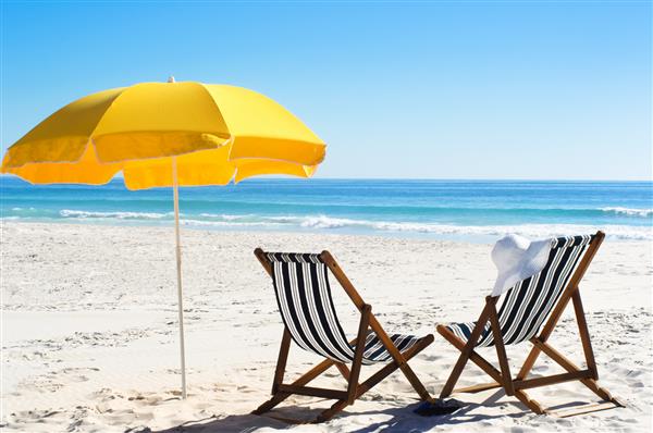 صندلی های ساحلی و چتر زرد در ماسه با نور آفتاب روشن
