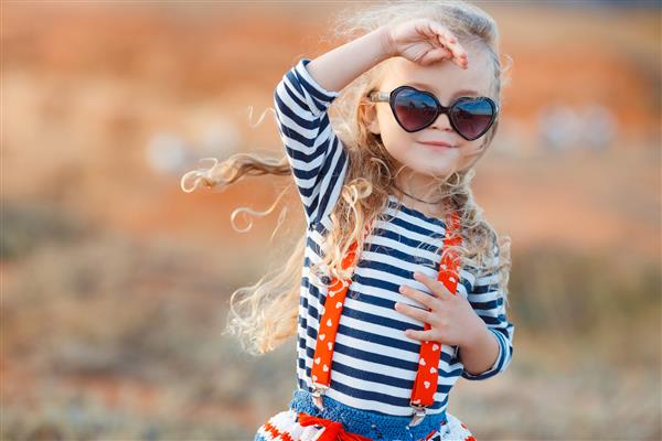 دختر کوچولوی شاد در کنار دریا در تابستان دختر کوچولوی شایان ستایش در ساحل در طول تعطیلات تابستانی کودک شاد با عینک آفتابی در کنار دریا یا اقیانوس