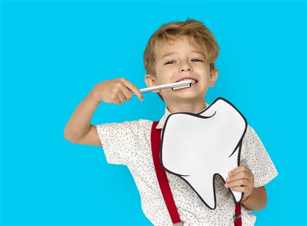 پسر کوچولو مسواک می‌زند که دندان‌های کاغذی را نگه می‌دارد