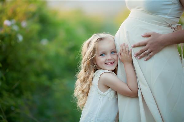 زن باردار شاد با دختر کوچک در باغ گل رز چای سبز
