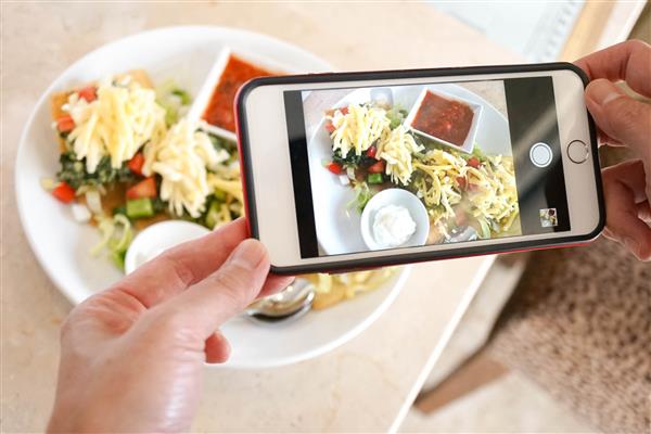 عکاسی از غذا از روی تاکو اسفناج با پنیر دست خانمی که گوشی هوشمند در دست دارد مفهوم رژیم غذایی سالم غذای گیاهی