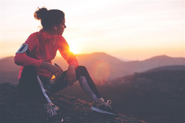 زن ورزشکار در حال استراحت پس از یک تمرین سخت در کوه در غروب آفتاب لباس های تنگ اسپرت