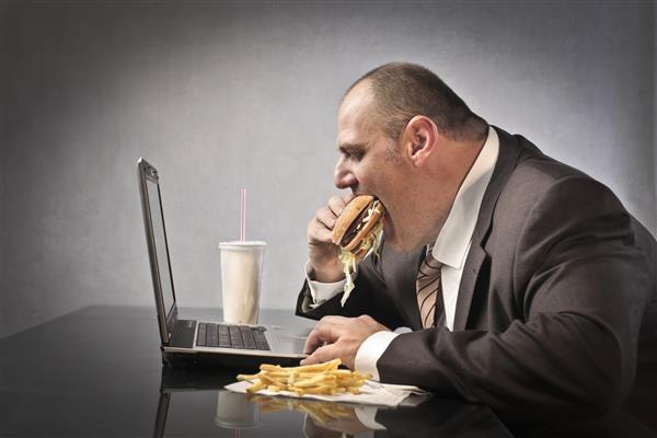 تاجر چاق در حال خوردن غذاهای ناسالم هنگام کار