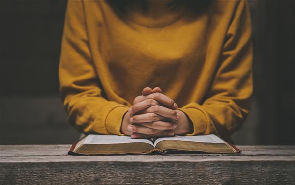 زنی در حال دعا بر روی کتاب مقدس در صبح دست در دست دعا روی میز چوبی دعای بحران زندگی مسیحی به خدا دست‌های روی انجیل مقدس در مفهوم کلیسا برای ایمان در دعا جمع شده است