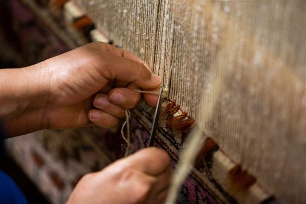 زن آذربایجانی قفقازی در حال بافتن یک فرش سنتی رنگارنگ با تکنیک های سنتی روی ماشین بافندگی با دست زیور شرقی نمای کناری نزدیک