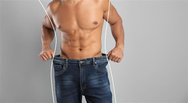 نمای نزدیک مرد با بدن عضلانی در شلوار جین بزرگ در پس زمینه خاکستری فضایی برای متن کاهش وزن