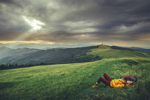 گردشگر زن آرامی که روی تپه دراز کشیده در حالی که از هوای تازه لذت می برد