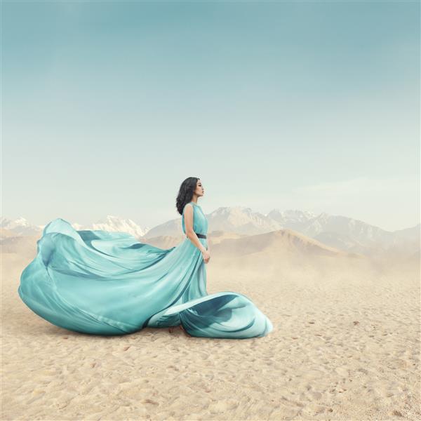 پرتره زن جوان زیبا با لباس بال بال بلند که در فضای باز در صحرای شنی ژست گرفته است