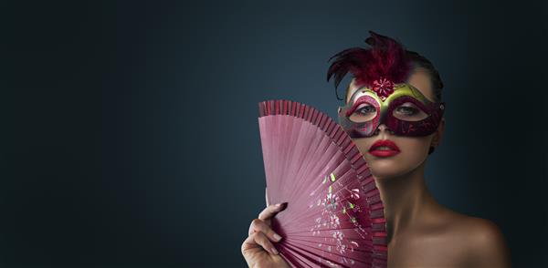 زن مدل لباس زیبایی که ماسک کارناوال بالماسکه ونیزی را در مهمانی روی پس زمینه تیره پوشیده است