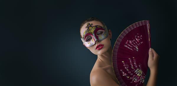 زن مدل لباس زیبایی که ماسک کارناوال بالماسکه ونیزی را در مهمانی روی پس زمینه تیره پوشیده است