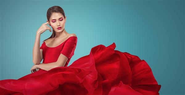 عکس استودیویی از زن جوان با لباس قرمز بلند زیبا که روی باد بال می زند
