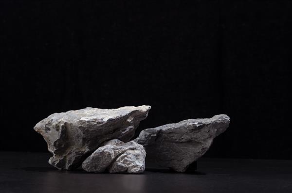 سنگ خاکستری طبیعی خشن به عنوان سکو برای بسته بندی و ارائه لوازم آرایشی در پس زمینه مشکی فضای کپی