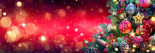 درخت کریسمس در پس زمینه قرمز براق - زیور آلات روی شاخه های صنوبر با نورهای انتزاعی درخشان و غیر متمرکز