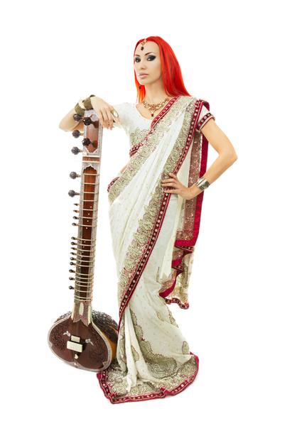 زن جوان سکسی مو قرمز با لباس ساری سنتی هندی با جواهرات شرقی و آرایش عروس در حال نواختن راگا سیتار دختر زیبای داغ بالیوود موسیقی شرقی