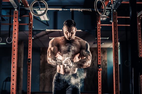 مرد عضلانی قوی برای تمرین در سالن کراس فیت آماده می شود ورزشکار جوان در حال تمرین تمرین کراس فیت