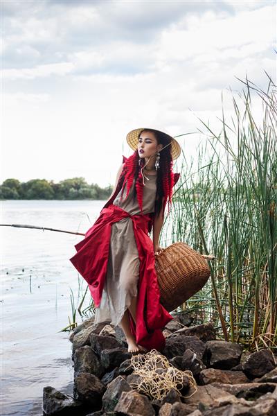 زن زیبا با کلاه به سبک آسیایی در کنار رودخانه