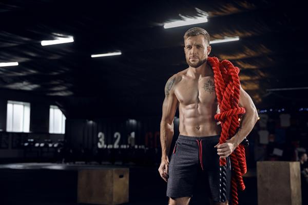 مرد جوان سالم ورزشکاری که با طناب در سالن بدنسازی ژست گرفته است