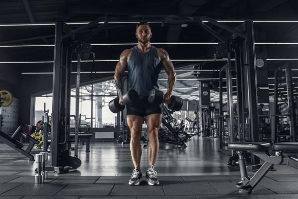 ورزشکار جوان عضلانی قفقازی در حال تمرین در سالن بدنسازی با وزنه ها