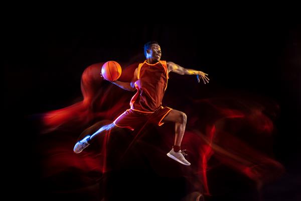 هدف را ببینید بسکتبالیست جوان آفریقایی-آمریکایی تیم قرمز در اکشن و نورهای نئون روی پس زمینه تیره استودیو مفهوم ورزش حرکت انرژی و پویا سبک زندگی سالم