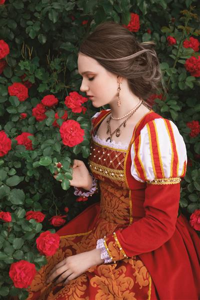 زن جوان با لباس قرمز قرون وسطایی در حال بوییدن گل رز است