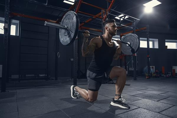 ورزشکار قفقازی قوی‌تر و عضلانی در حال تمرین لانژ در سالن بدنسازی با هالتر مدل مرد در حال انجام تمرینات قدرتی تمرین پایین تنه خود تندرستی سبک زندگی سالم مفهوم بدنسازی