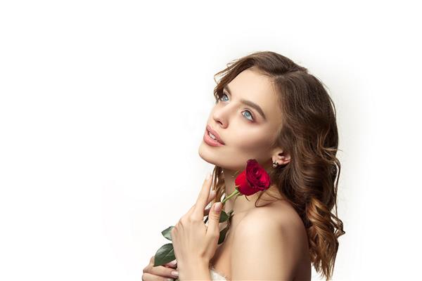 زن جوان خندان زیبا با موهای ابریشمی مواج بلند آرایش طبیعی با گل رز قرمز جدا شده روی دیوار سفید مدل با پوست براق تازه و آرایش طبیعی احساسات مردم