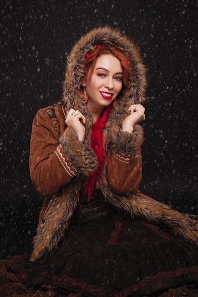 زن با کت خز به سبک قومی نشسته در برف در حال سقوط