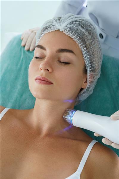 زن زیبا در حین درمان لیفت با فرکانس رادیویی روی گردن خود در یک کلینیک زیبایی پزشکی